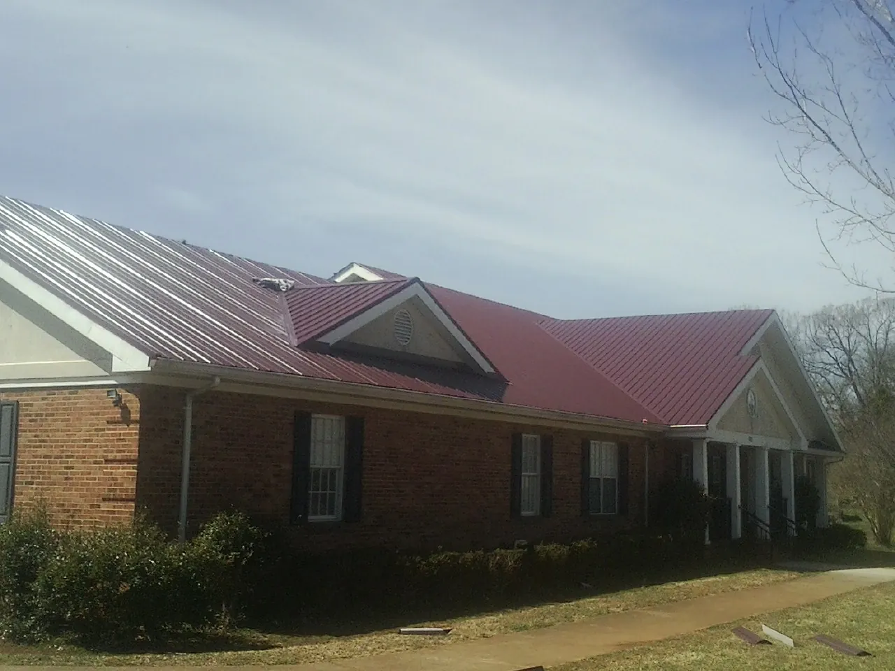 Red metal roof with gabled entries on a long brick building, from a Hail Damage Roof Repair job in Tecumseh