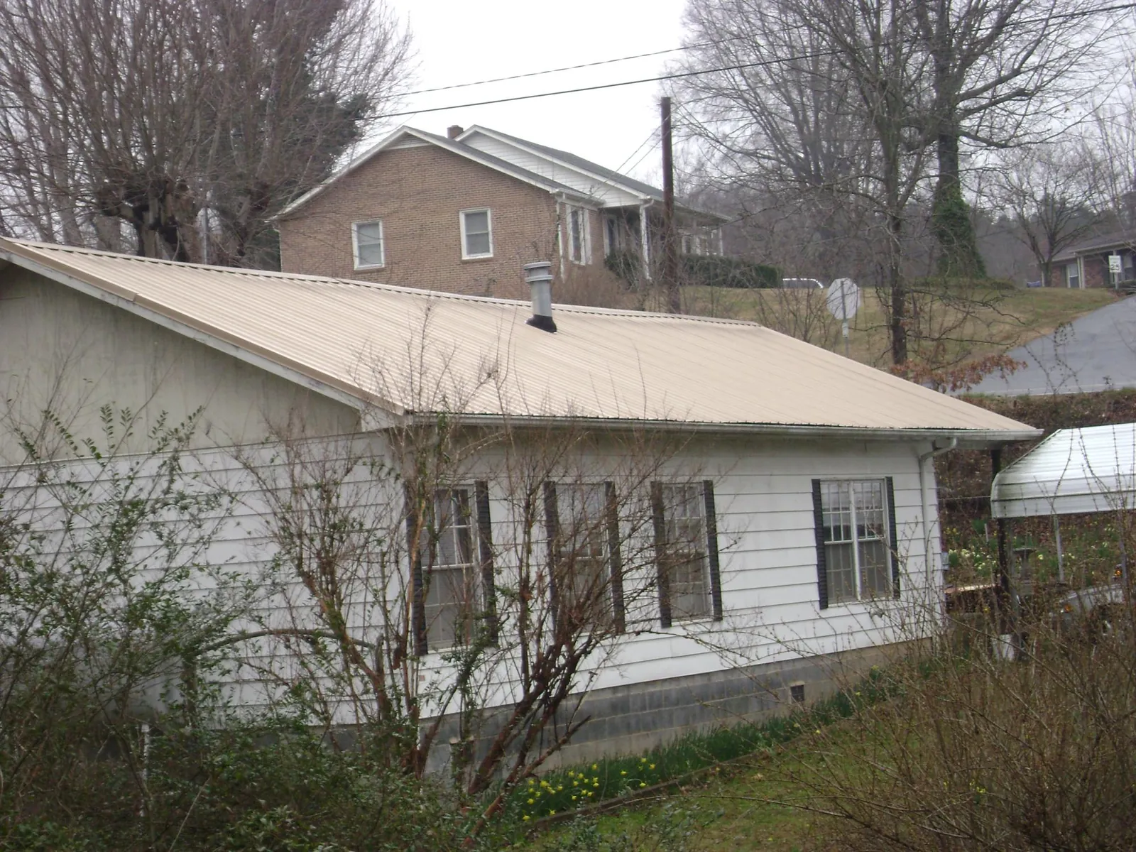 Tan metal roof on a white sided house set into a hillside — Commercial Roofing by Roofing Brothers in Tecumseh