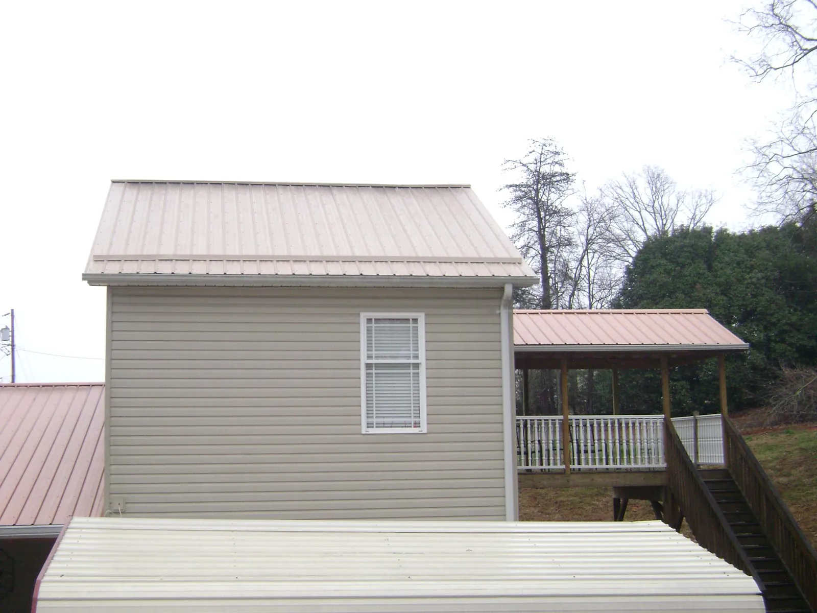 Tan metal roofs on a two story addition and attached porch, from a Roof Replacement job in Tecumseh
